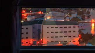 A picture of a city through a window at night, with Jill's reflection faintly visible